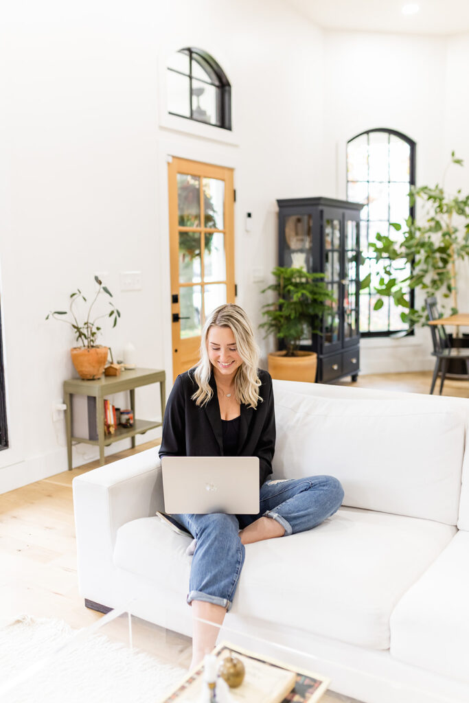 woman sitting on couch writing goals for second half of the year on her laptop