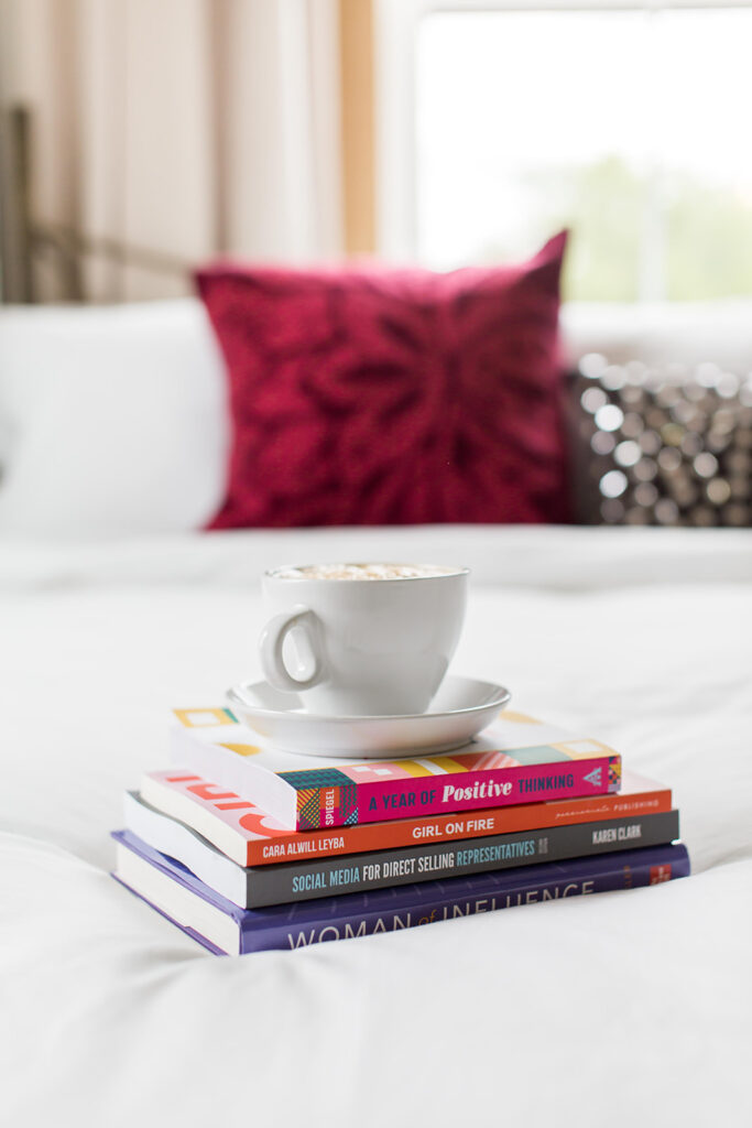 a pile of books on the bed with a coffee on top