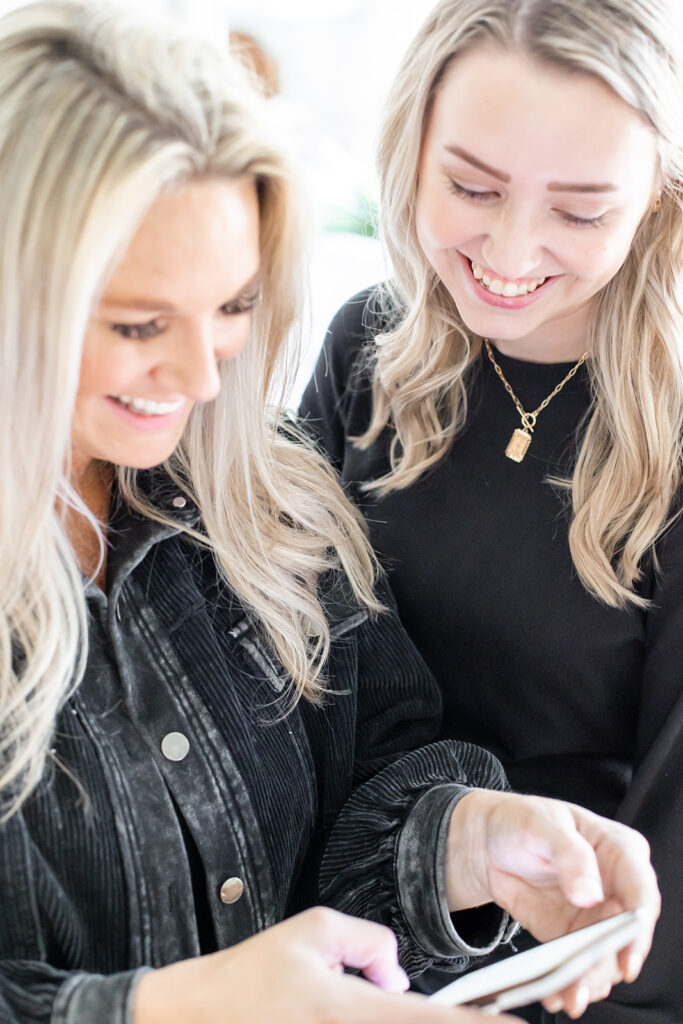 two women dressed in black smiling at phone