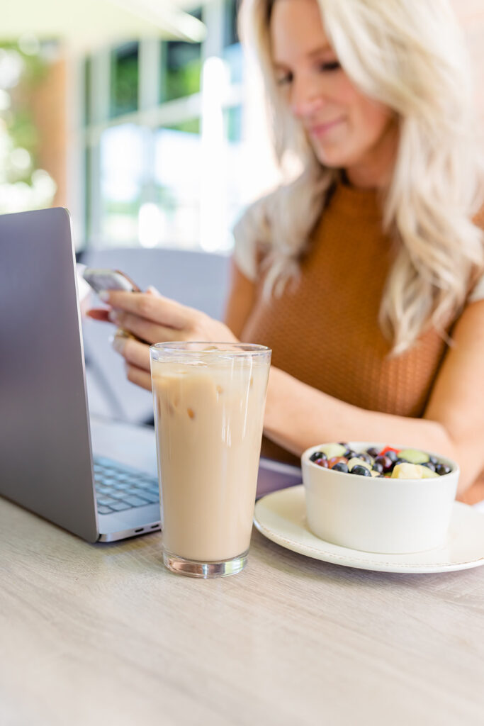 woman working on laptop at coffee shop holding iphone