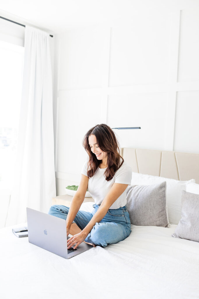 smiling woman sitting on bed working on laptop