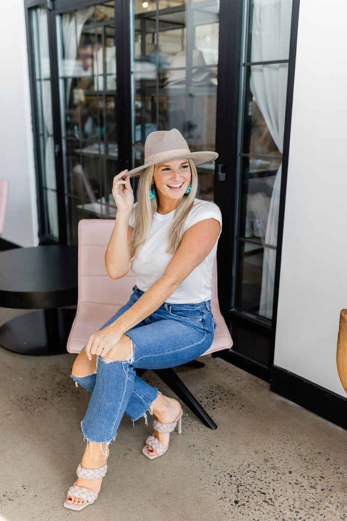 happy woman sitting on chair with cowboy hat and neutral heels