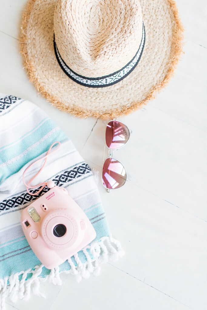 pink Fujifilm camera with sunglasses, hat, and towel