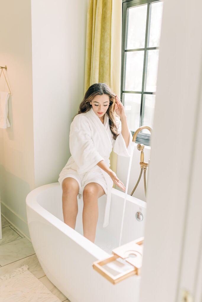 woman in robe sitting on tub with running water