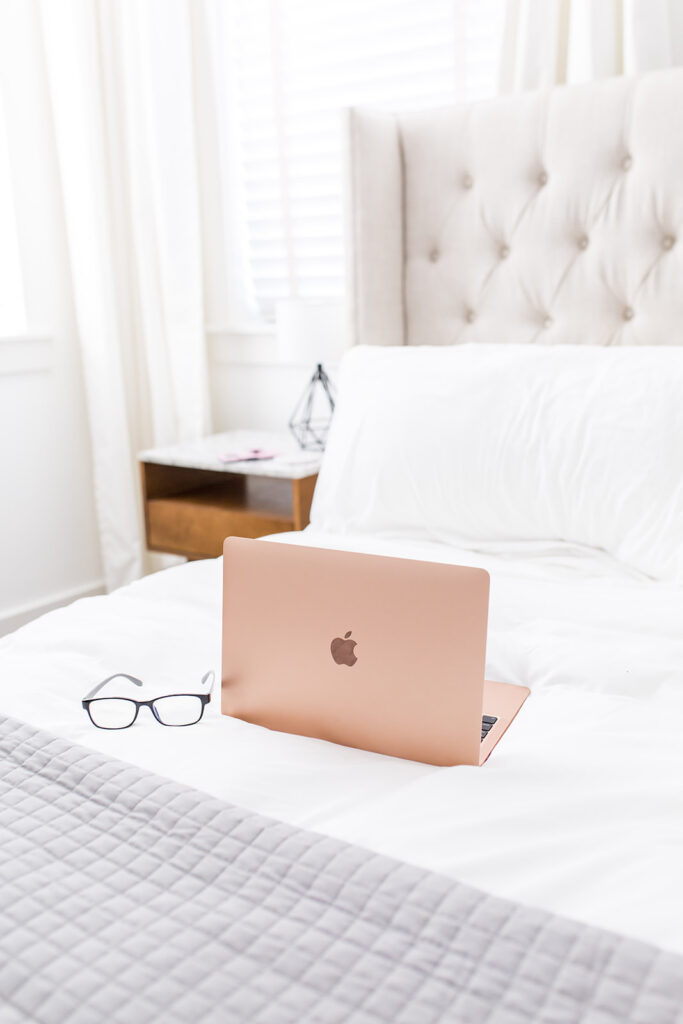 pink laptop and glasses on bed