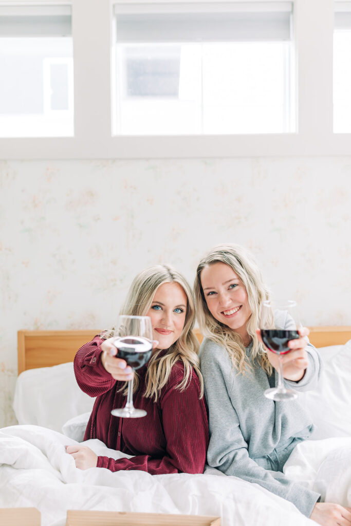 two girls in pajamas holding red wine glasses in bed