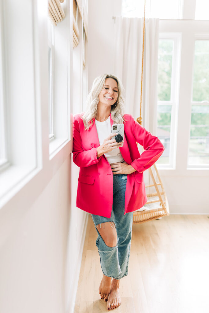 successful woman holding phone in pink blazer and jeans