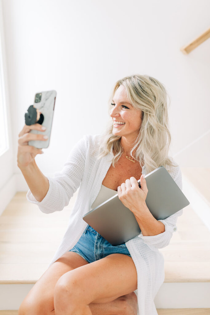 smiling woman taking selfie holding laptop