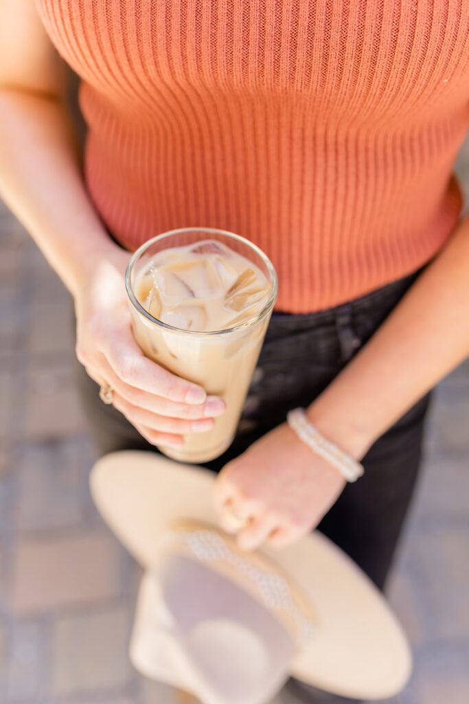 woman in orange holding iced coffee and hat